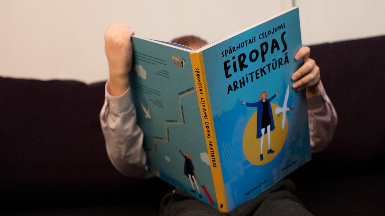 Grāmatas “Spārnotais ceļojums Eiropas arhitektūrā” atvēršanas svētkos mazs zēns iegrimis grāmatas pētīšanā