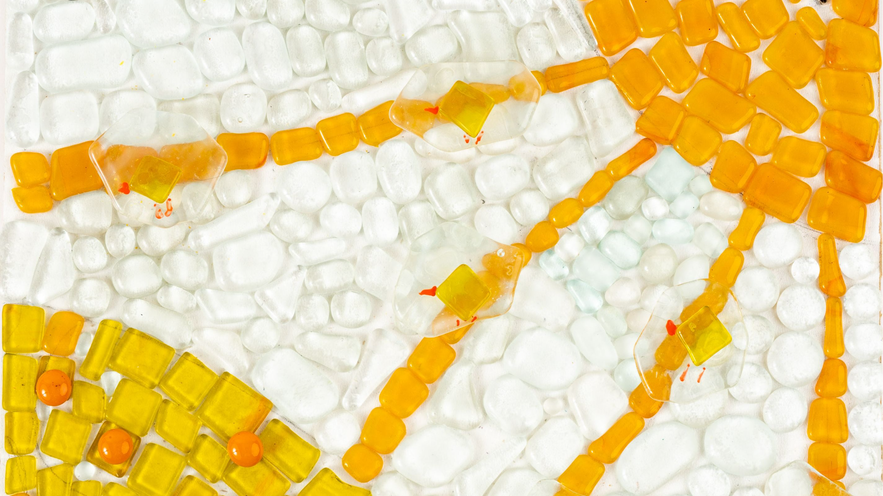 Stikla gabaliņu mozaīkā veidots darbs ar caurspīdīgi baltu fonu, dzeltenu sauli un dzeltenu zemi 