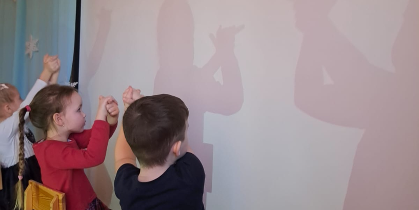 Bērni ar rokām uz ekrāna rāda ēnu teātri