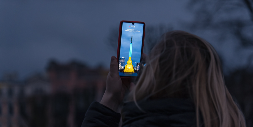 Sieviete fotografē Brīvības pieminekli, kas izgaismots Ukrainas karoga krāsās