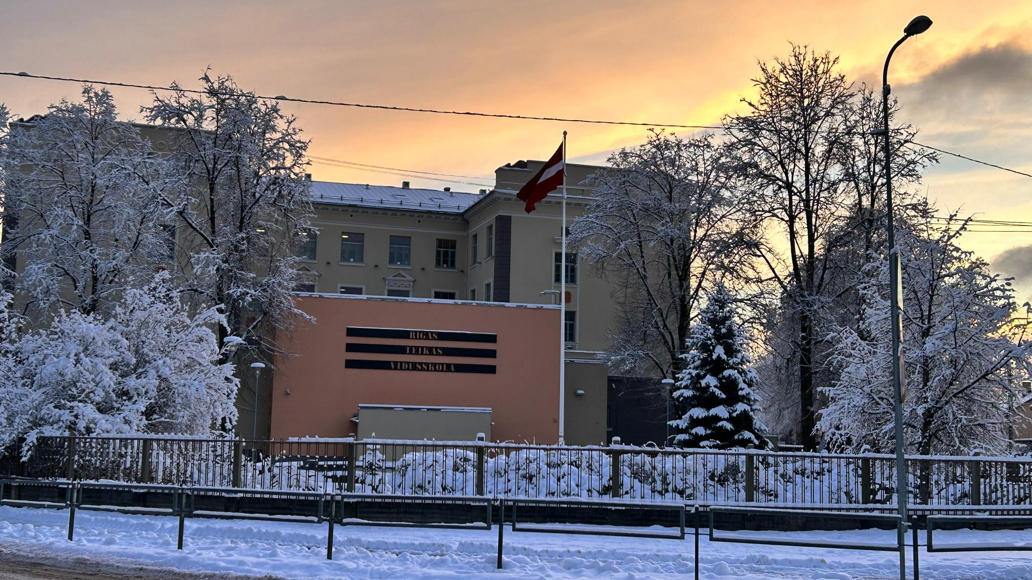 Rīgas Teikas vidusskolas ēka ziemā uz saulrieta fona
