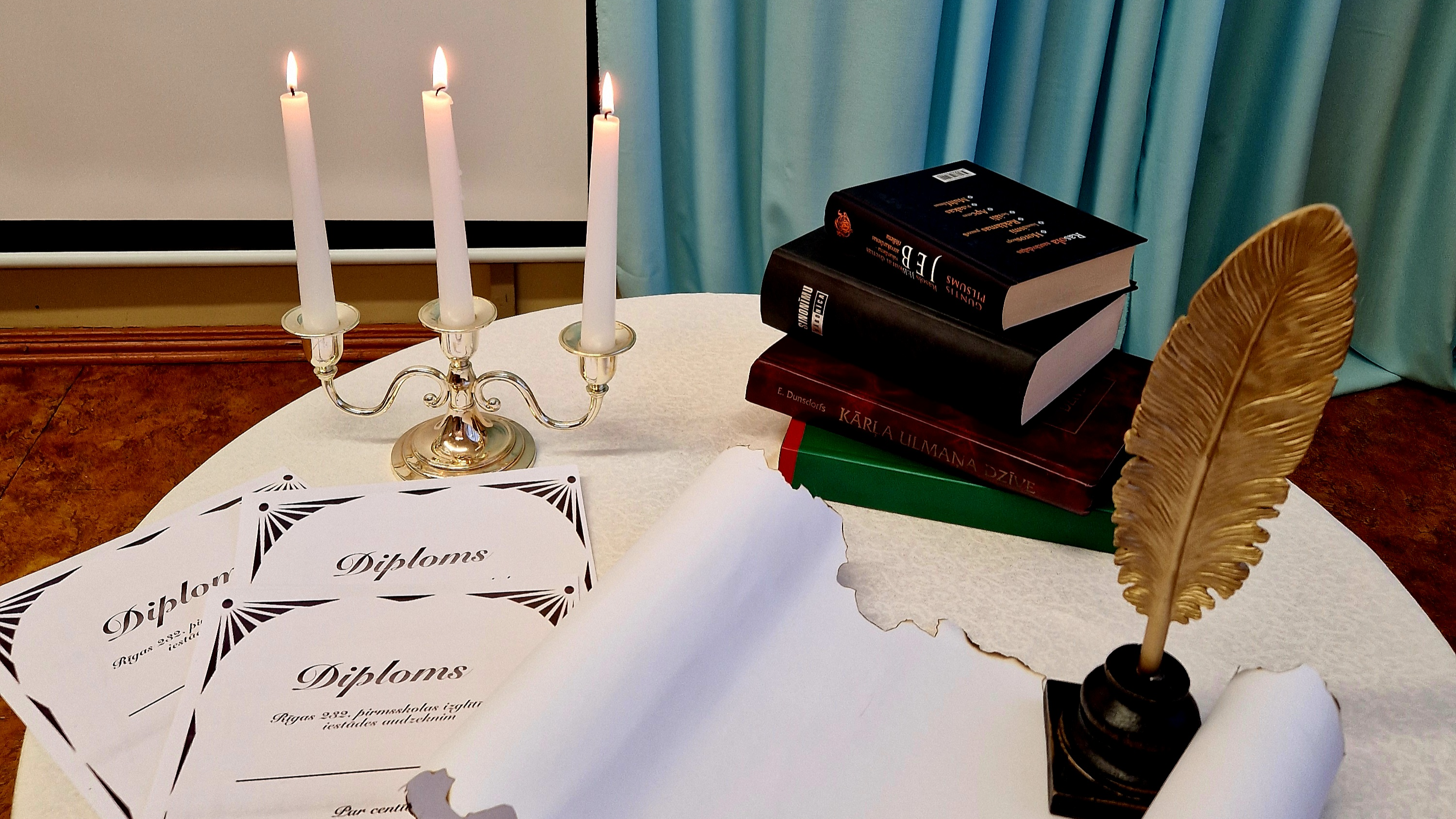 Dzejoļu konkursa noformējums ar grāmatām, diplomiem, rakstāmspalvu un degošām svecēm svečturī