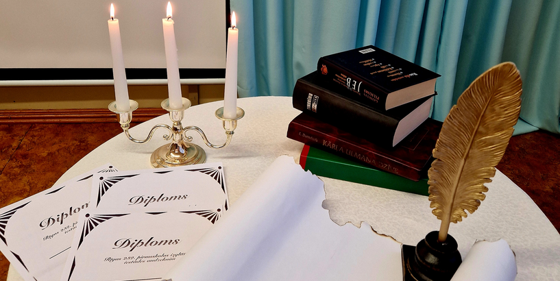 Dzejoļu konkursa noformējums ar grāmatām, diplomiem, rakstāmspalvu un degošām svecēm svečturī