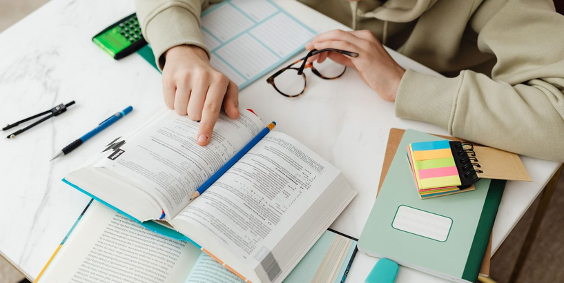 Jaunietis pie galda ar grāmatām un kladēm pilda uzdevumus