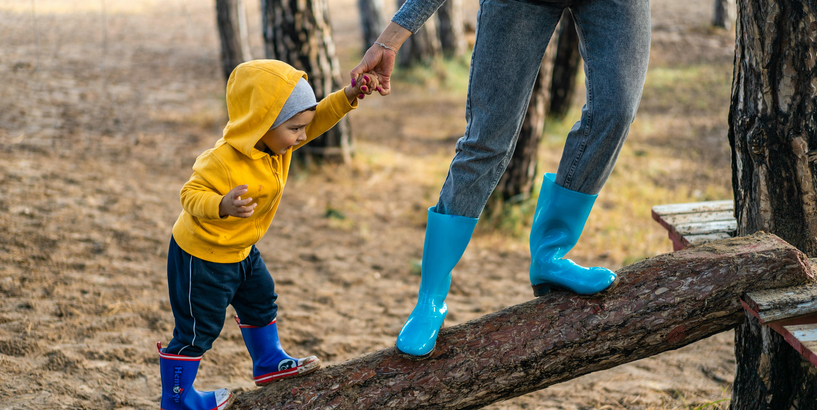 Bērns, turoties pie sievietes rokas, cenšas uzkāpt pa baļķi