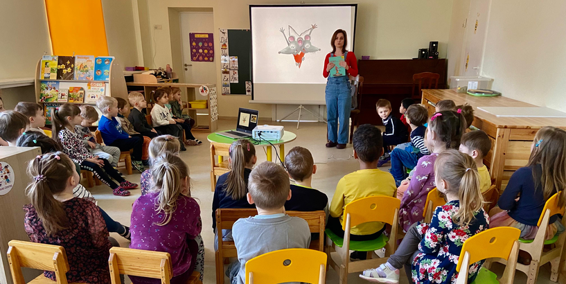 Bērnudārza bērni sēž aplī un klausās rakstnieces Evijas Gulbes stāstītajā