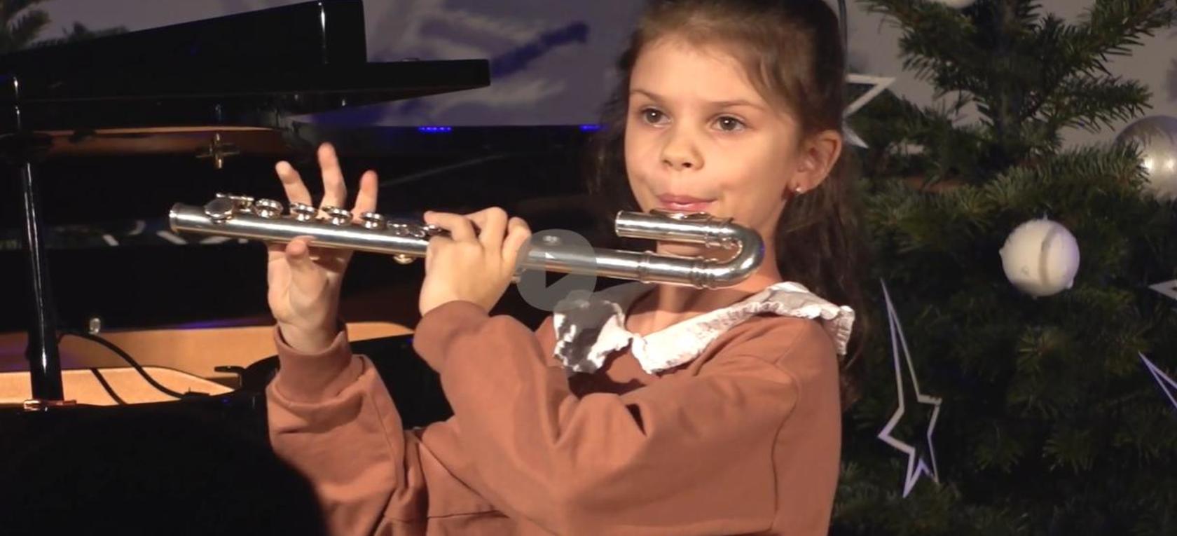 Ziemassvētku eglītes fonā mūzikas skolas audzēkne spēlē flautu